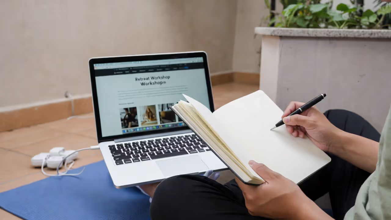 Person researching yoga retreat options with notebook and laptop in calm setting