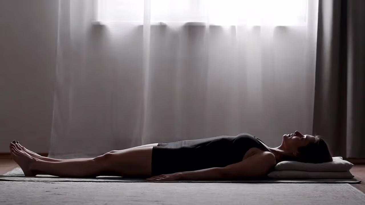 Person resting in a supported yoga relaxation pose on a mat in a calm room