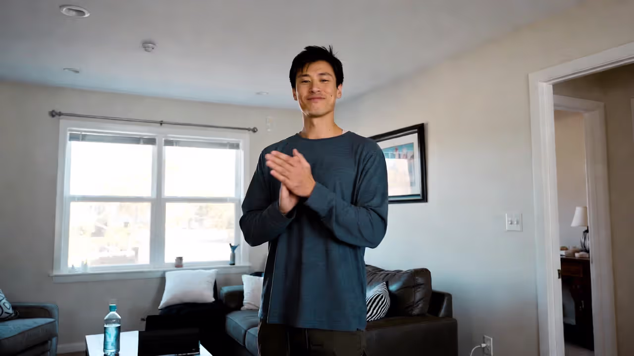 Person practicing laughter yoga at home with open space and water nearby.
