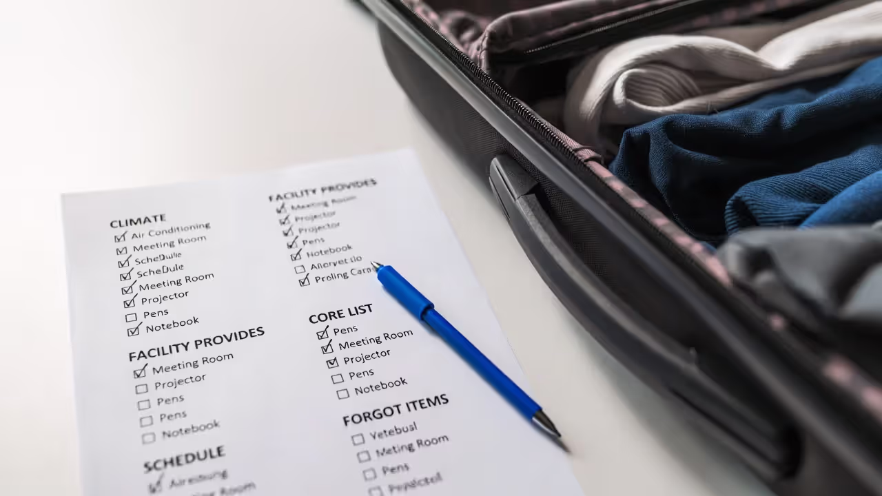 Printed packing checklist beside a partially packed suitcase and pen.
