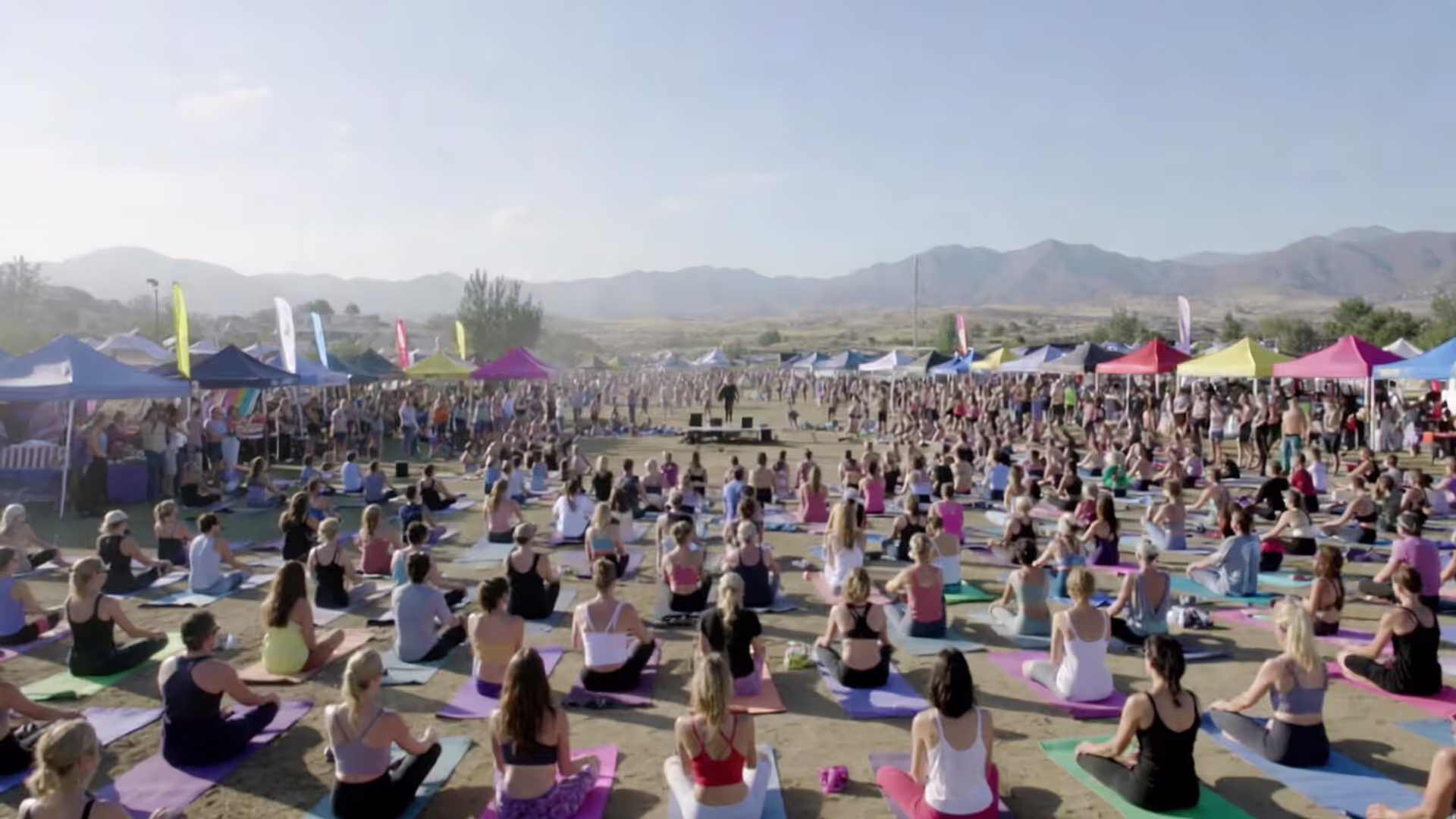 Large outdoor yoga festival with hundreds of participants practicing in front of a stage.